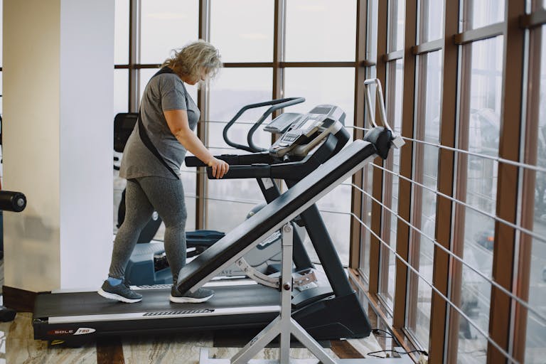 Adult woman exercising on a treadmill in a bright, modern gym setting.