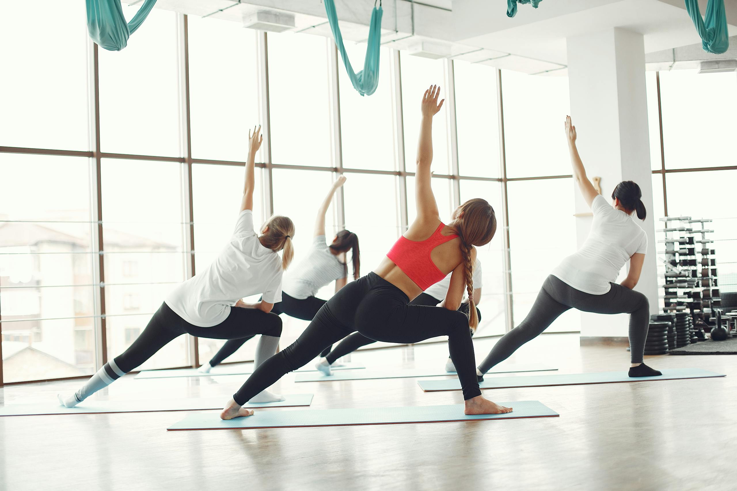 Diverse group of women practicing yoga in a well-lit gym with large windows.