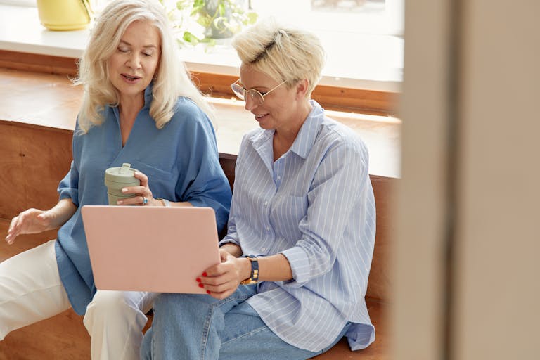 Two senior women discussing ideas over a laptop, conveying teamwork in a casual business setting.