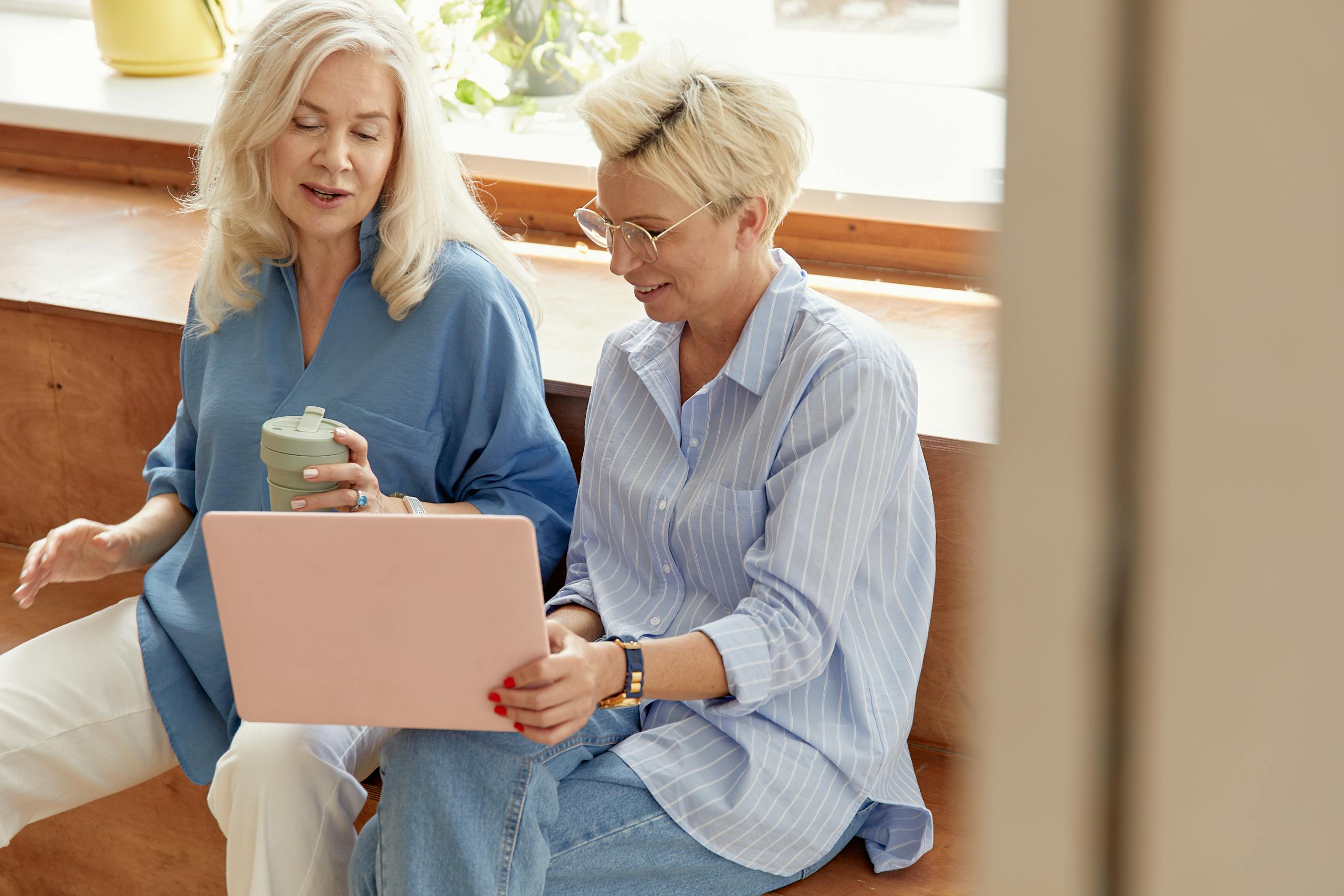 Two senior women discussing ideas over a laptop, conveying teamwork in a casual business setting.